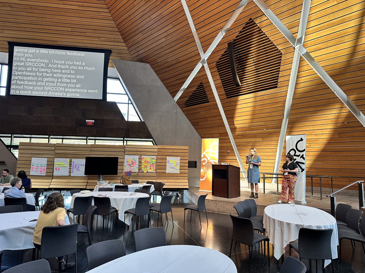 text on a big screen with two people standing before a conference hall