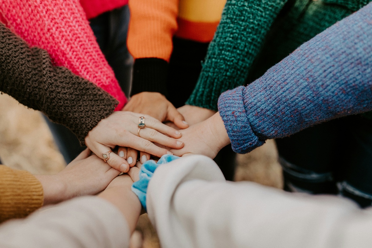 A stock image of a group of different hands coming together in the middle of a group of people, a common team-building or cheering practice denoting unity and a common cause.